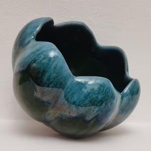 Peut inclure: Un bol en céramique de couleur sarcelle avec une forme ondulée et organique. La surface brillante présente des variations de couleur, allant du sarcelle foncé aux nuances bleu-vert plus claires. L'intérieur est d'une teinte sarcelle plus foncée.