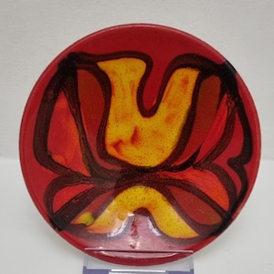 May include: A circular ceramic bowl with a bright red exterior. The interior showcases a striking abstract design in yellow, orange, and brown, outlined with dark brown lines. The bowl's design is centrally placed, creating a strong visual contrast.