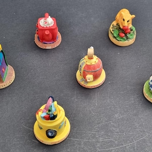 Peut inclure: Cinq théières miniatures en céramique avec des motifs différents. Les théières sont sur une surface grise. Les théières sont décorées de différentes couleurs et motifs, notamment le rouge, le jaune, le bleu, le vert et le brun.