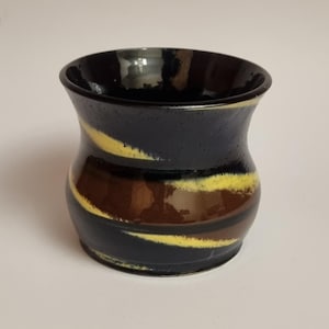 Peut inclure: Un vase en céramique fait à la main avec un extérieur bleu foncé, orné de bandes horizontales marron et jaune. Le vase a un corps arrondi et un bord légèrement évasé, idéal pour la décoration intérieure.