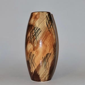 Peut inclure: Un vase cylindrique aux extrémités effilées, orné d'un motif peint à la main composé de coups de pinceau diagonaux marron et beige, superposés de lignes croisées brun foncé. La surface présente une finition lisse et brillante sur tout l'extérieur.