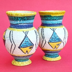 May include: Two small ceramic vases with a textured white surface, featuring hand-painted blue and yellow triangular motifs. The rims and bases are painted in yellow, with horizontal bands of teal, blue, and yellow encircling the neck and base.