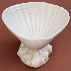 May include: White ceramic seashell dish with a textured surface and a base shaped like a rock. The dish is ideal for holding small items such as jewellery or trinkets.