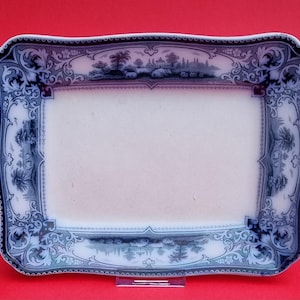 Peut inclure: Un plat de service rectangulaire blanc avec un motif floral bleu et blanc autour du bord. Le plat a un bord festonné et un rebord surélevé.