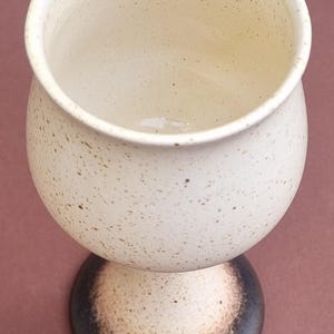 Peut inclure: Un gobelet en céramique blanche avec un glaçage moucheté et une base noire. Le gobelet a un bol large et rond et une tige haute et mince.