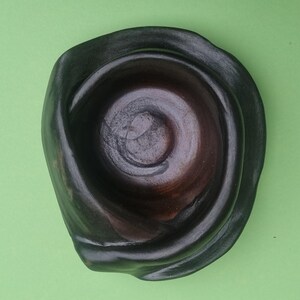 Peut inclure: Un bol en céramique brun foncé avec un glaçage noir. Le bol a une forme organique unique et une surface légèrement texturée.