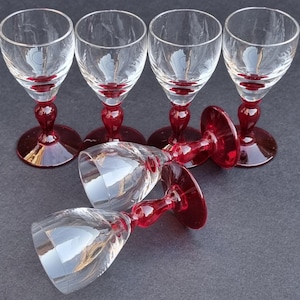 May include: Set of six clear glass shot glasses with red bases. The glasses have a delicate design and are perfect for serving small drinks.