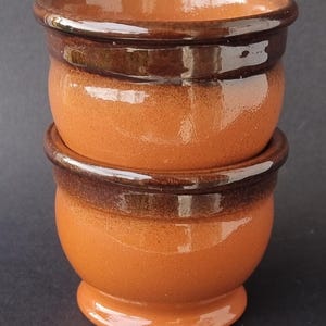 Op de afbeelding: Twee terracotta potten met een bruine glazuur rond de rand. De potten zijn op elkaar gestapeld.