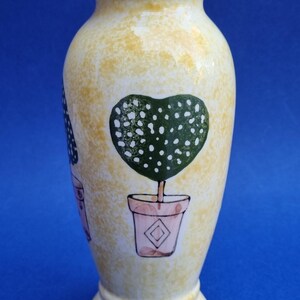 Peut inclure: Un vase décoratif en céramique avec un fond jaune moucheté. Le vase présente un motif d'arbre en forme de cœur dans un pot rose. Le vase mesure environ 20 cm de haut.