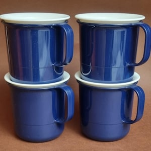 May include: Four navy blue mugs with white rims and handles are stacked in two pairs. The mugs have a classic design, suitable for hot or cold drinks. The mugs are made of a durable material.