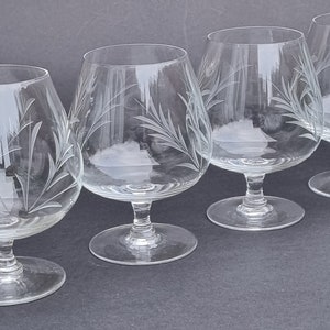 Op de afbeelding: Vier heldere glazen brandy snifters met gegraveerde bladmotieven. De glazen hebben een ronde kom en een lange, slanke steel.