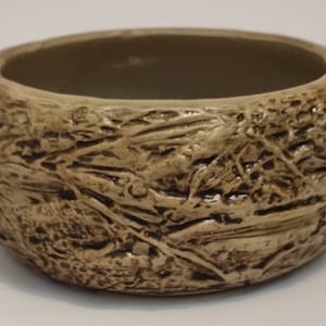 Op de afbeelding: Een kleine, ronde, bruine keramische pot met een getextureerd oppervlak dat lijkt op boomschors.