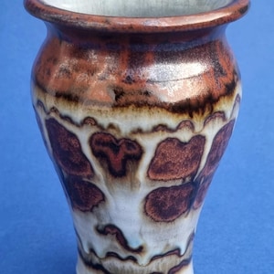 Peut inclure: Un petit vase en céramique brun et blanc avec un design abstrait unique. Le vase a une base arrondie et une ouverture étroite.