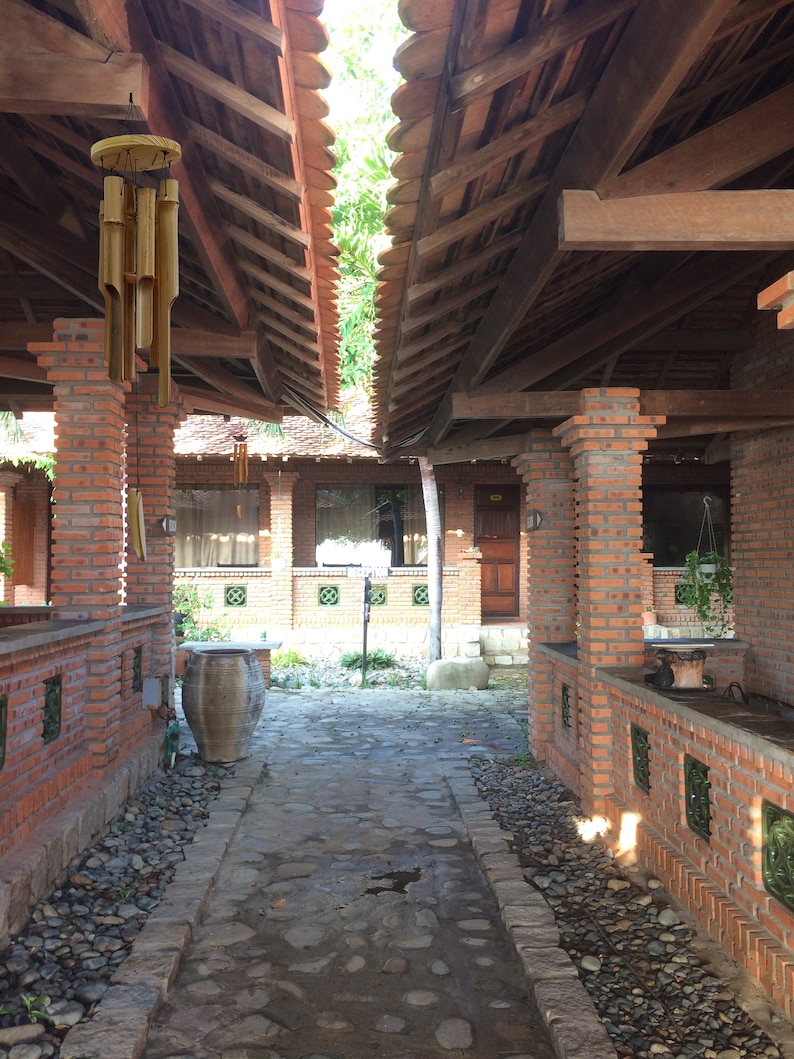 Puede incluir: Un camino de ladrillos con un sendero de piedra que conduce a una estructura de madera con techo de paja. Un carill&oacute;n de madera cuelga del techo de la estructura. El camino est&aacute; bordeado de peque&ntilde;as piedras.