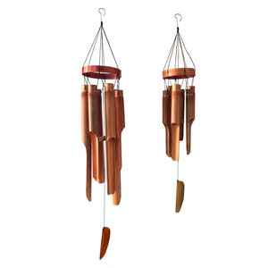 May include: Two brown bamboo wind chimes with a wooden ring at the top and a long, thin, brown piece of wood hanging from the bottom. The wind chimes are hanging from a white background.