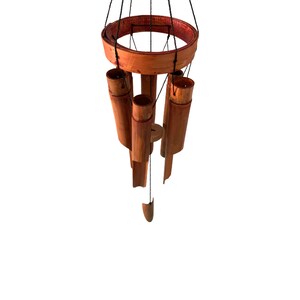 May include: A wooden wind chime with a circular top and five hanging tubes. The tubes are made of natural bamboo and are stained a reddish brown color. The wind chime is suspended from a black string.