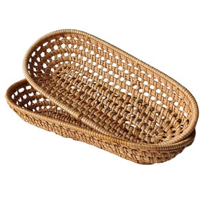 May include: A woven oval-shaped basket made of natural brown rattan. The basket is made of a tightly woven pattern and has a slightly rounded shape.