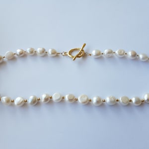 以下が含まれることがあります： 金色の留め具が付いた白い真珠のネックレス。真珠は形とサイズが不揃いです。