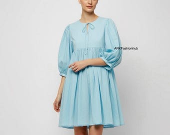 May include: A light blue dress with a round neckline and a tie detail. The dress features three-quarter length, puffed sleeves and a flared skirt. The text "ARKFashionhub" is visible on the right side of the image.