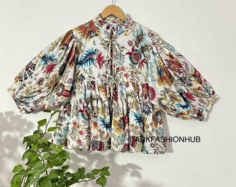 May include: A white blouse with a colorful floral pattern, featuring red, blue, and yellow accents. The blouse has a high collar, a tie detail, and puffy sleeves. The text "ARKFASHIONHUB" is visible on the bottom of the blouse.