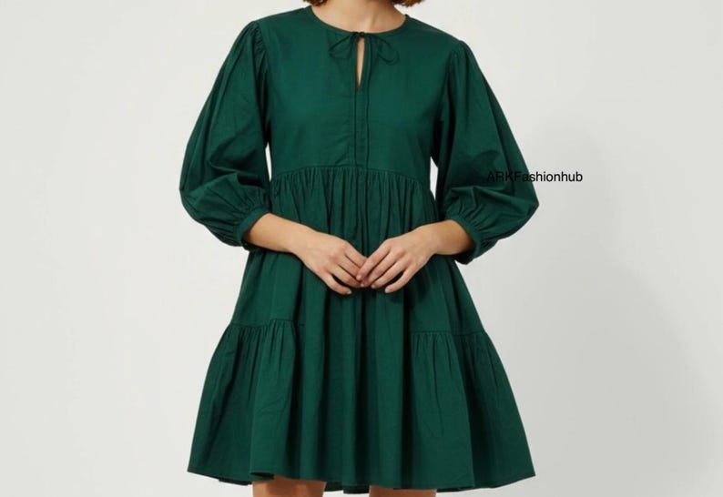 May include: A dark green dress with a round neckline and a keyhole detail. The dress features long, voluminous sleeves and a tiered skirt. The fabric appears to be a lightweight cotton or similar material. The dress has a relaxed, flowing silhouette.