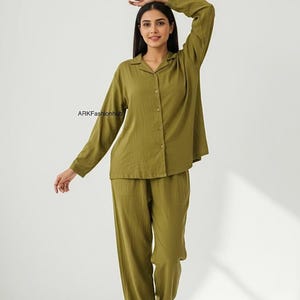 Può includere: Set pigiama verde oliva. Il set comprende una camicia abbottonata con colletto e maniche lunghe e pantaloni a gamba larga abbinati. Il tessuto sembra leggero e confortevole. Il nome del marchio "ARKFashionhub" è visibile sulla camicia.