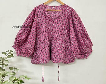 Op de afbeelding: Een roze katoenen blouse met een bloemenprint en pofmouwen. De blouse heeft een trekkoord aan de onderkant en een V-hals.