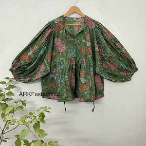 May include: A green floral print blouse with puffed sleeves and a gathered waist. The blouse has a V-neckline and a tie at the front.
