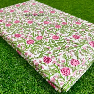 May include: Folded fabric with a floral pattern. The fabric has a white background with a repeating design of pink flowers and green leaves and vines. The text "ARKFASHIONHUB" is printed on the fabric.