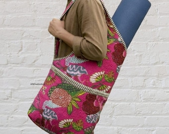 Puede incluir: Una bolsa acolchada para esterilla de yoga en tela rosa magenta vibrante con un patrón floral y abstracto multicolor. La bolsa tiene una correa ancha para el hombro y contiene una esterilla de yoga azul oscuro enrollada. El texto ARKFashionHub es visible.
