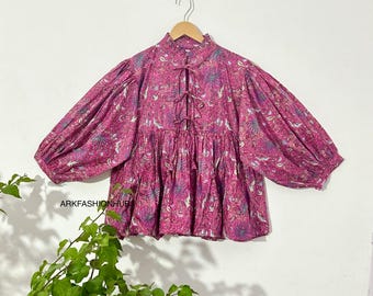 May include: A magenta-colored blouse with a floral pattern and long, voluminous sleeves. The blouse has a high neckline with a tie detail and is hanging on a wooden hanger. The text "ARKFASHIONHUB" is visible.