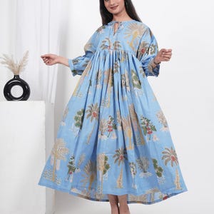 May include: A light blue maxi dress with a tie-up neckline and a floral print featuring palm trees and other plants. The dress has a gathered waist and 3/4 sleeves.