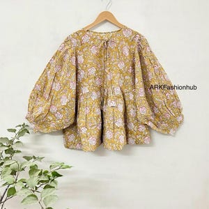 May include: A yellow and pink floral print blouse with puffed sleeves. The blouse has a gathered waist and a tie at the neckline.