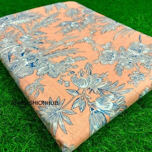 May include: Folded fabric with a floral pattern in peach, blue, and white. The fabric features a repeating design of stylized flowers and foliage. The text "ARKFASHIONHUB" is visible in the lower left corner.