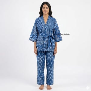 Può includere: Un set di kimono e pantaloni abbinati con motivi blu e bianchi. L'accappatoio, in stile kimono, è incrociato e ha una cintura. I pantaloni sono dritti. Il tessuto presenta vari motivi geometrici e floreali bianchi su sfondo blu.