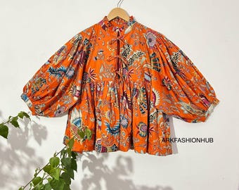 May include: Orange blouse with a floral pattern and long, voluminous sleeves. The blouse has a high neckline with a tie closure and a gathered waist. The fabric is adorned with a colorful, intricate design. The text "ARKFASHIONHUB" is visible on the bottom right.