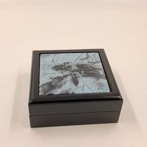 May include: Black wooden box with a light blue and black abstract design on the lid.