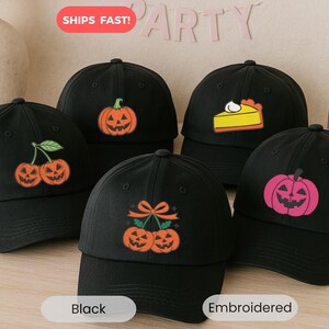 May include: Black baseball caps with embroidered Halloween-themed designs. The designs include jack-o'-lanterns, cherries, and a slice of pie. The caps are a classic baseball style.