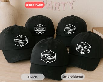 May include: Black baseball caps with white embroidered text, including "Groom," "Best Man," "Groomsman," and "Father," with dates. The caps are a wedding party theme.