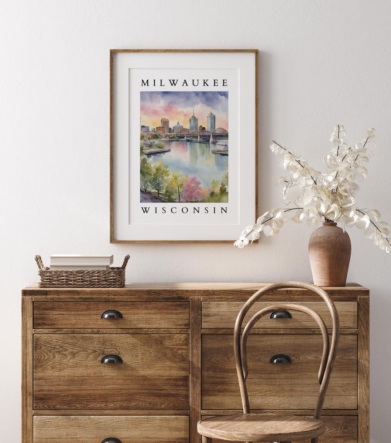 A Milwaukee, Wisconsin cityscape print in a wooden frame, elegantly placed above a rustic wooden dresser with white floral decor and a woven chair.