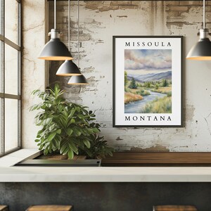 May include: A framed watercolor painting of a river scene with the text "Missoula Montana" at the top and bottom. The painting depicts a river winding through a green valley with mountains in the background.