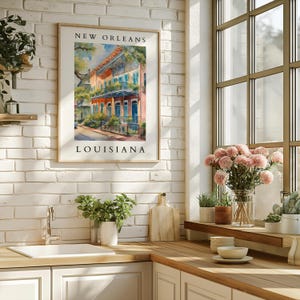 May include: A watercolor painting of colorful buildings in New Orleans, Louisiana. The painting is framed and hanging on a white brick wall in a kitchen.
