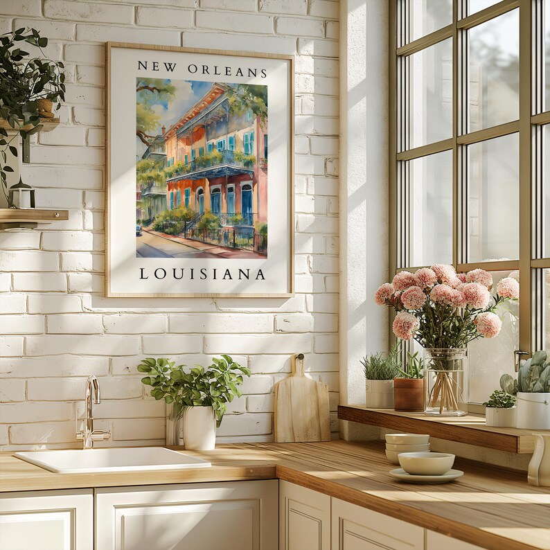 May include: A watercolor painting of colorful buildings in New Orleans, Louisiana. The painting is framed and hanging on a white brick wall in a kitchen.