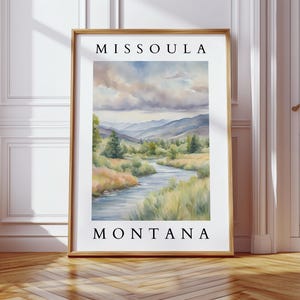 May include: A watercolor painting of a river flowing through a valley with mountains in the background. The painting is framed and has the text "Missoula Montana" at the top and bottom.