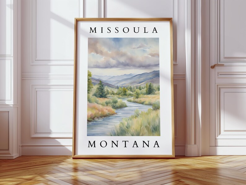 May include: A watercolor painting of a river flowing through a valley with mountains in the background. The painting is framed and has the text "Missoula Montana" at the top and bottom.