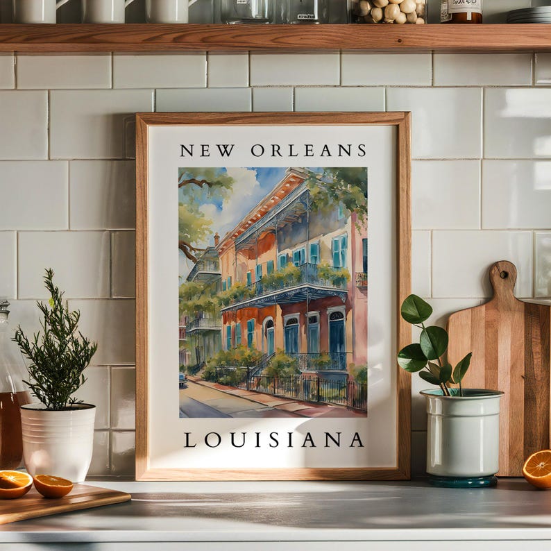 May include: A framed watercolor painting of a colorful building in New Orleans, Louisiana. The building has a balcony and is surrounded by lush greenery. The text "NEW ORLEANS" and "LOUISIANA" is printed below the image.