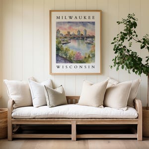 A Milwaukee cityscape watercolor print framed above a light-colored sofa with soft neutral pillows, surrounded by plants and natural elements.