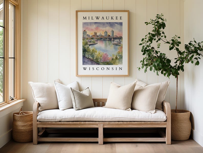 A Milwaukee cityscape watercolor print framed above a light-colored sofa with soft neutral pillows, surrounded by plants and natural elements.