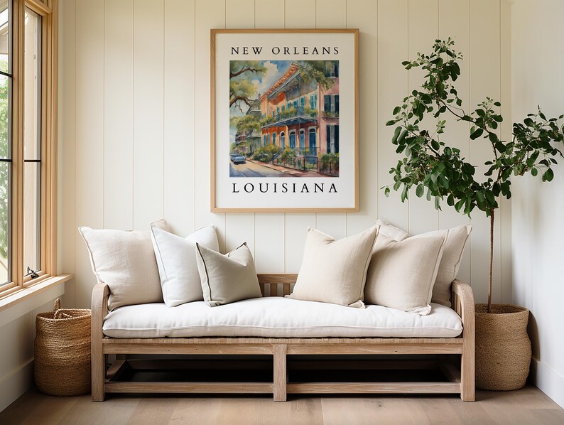 May include: A white linen bench with pillows sits in front of a white wall with a framed print that reads "NEW ORLEANS LOUISIANA". A potted plant with green leaves is on the right side of the image.