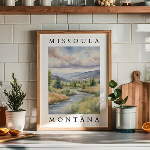 May include: A framed watercolor painting of a river winding through a valley with mountains in the background. The painting is titled "Missoula, Montana".